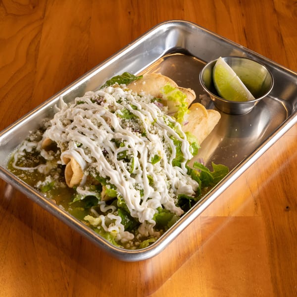 Mi Sabor Mexican Kitchen's taquitos with green sauce, lettuce, cheese, and crema, served with lime wedges.