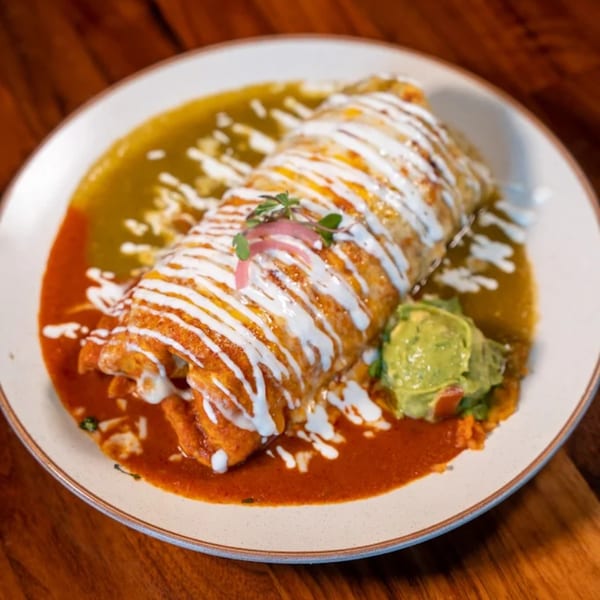 Mi Sabor Mexican Kitchen's burrito covered in red and green sauce, drizzled with crema, and served with guacamole.