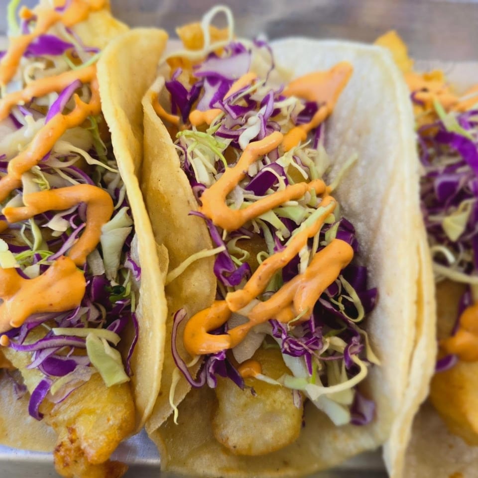 Three Mi Sabor Mexican Kitchen fish tacos with shredded cabbage and orange sauce.