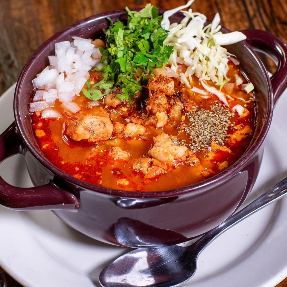 A bowl of Mi Sabor Mexican Kitchen's pozole with chicken, onions, cilantro, and cabbage.