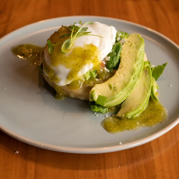 Mexican dish with a poached egg, green sauce, sliced avocado, and greens on a light blue plate.