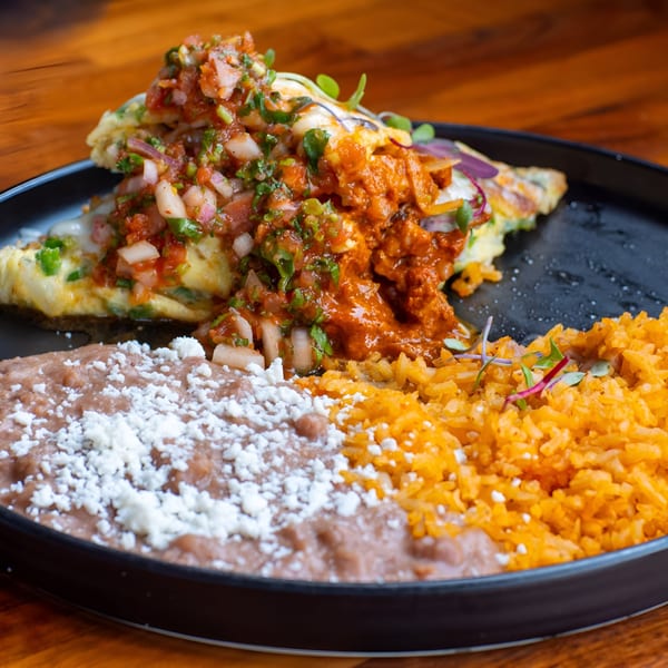 Mi Sabor Mexican Kitchen's huevos rancheros with salsa, chorizo, refried beans, and rice on a black plate.