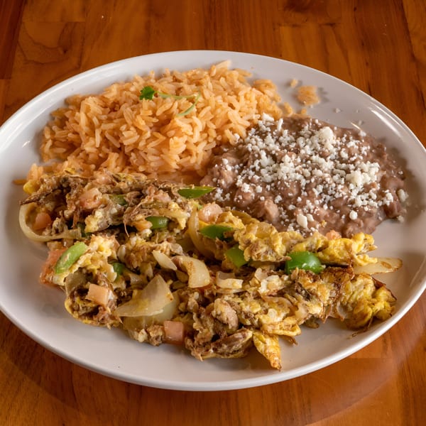 A white plate of Mi Sabor Mexican Kitchen's scrambled eggs with beef, rice, and refried beans.