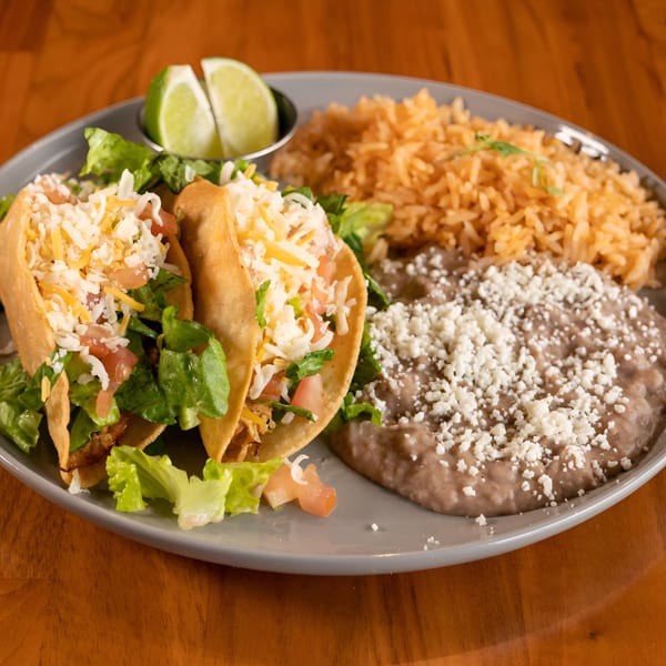 Two Mi Sabor Mexican Kitchen tacos with rice, refried beans, and lime wedges on a gray plate.