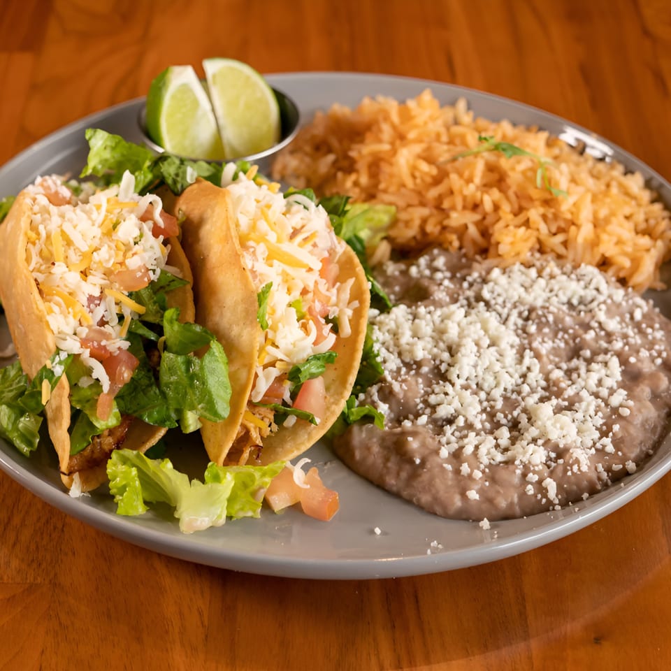 Two Mi Sabor Mexican Kitchen tacos with rice, refried beans, and lime wedges on a gray plate.
